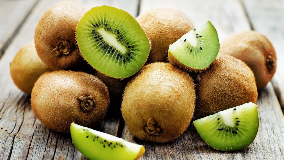 A pile of kiwi, some whole and unpeeled, others cut into wedges