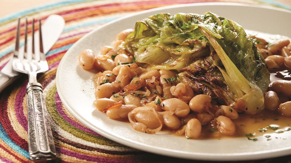 A while plate with braised lettuce and beans next to a fork on a colorful placemat. 