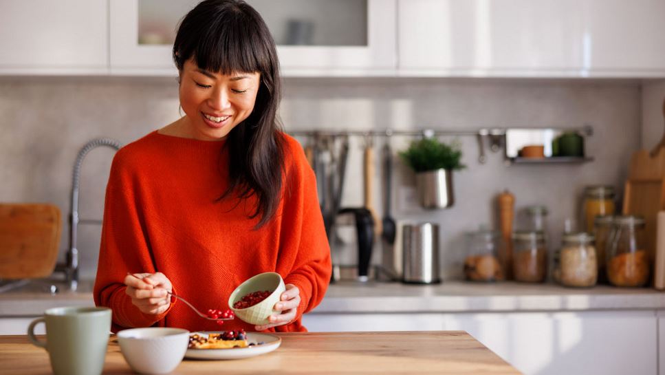 Woman spooning fruit over her breakfast in a clean and modern kitchen