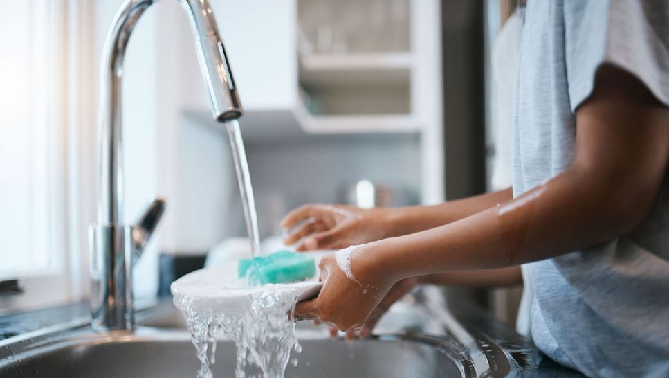 Handwashing dishes under running water with a sponge