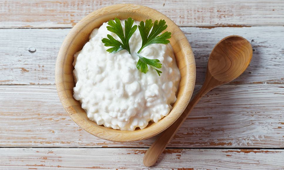 Plain small curd cottage cheese in a bowl with a wooden spoon